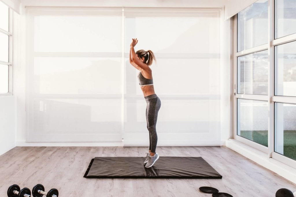 Woman in home studio space doing burpees