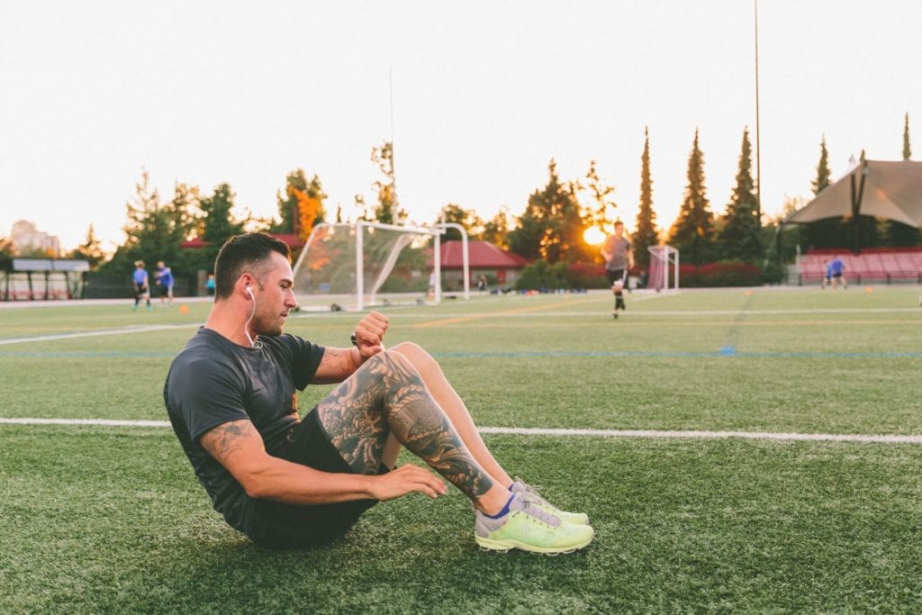 Man in park doing sit-ups checking his heart rate watch